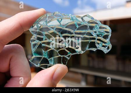 En tenant le bout des doigts un morceau de verre trempé, verre trempé vert cassé. Pièce de verre fissurée. Banque D'Images