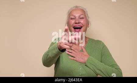 Femme caucasienne âgée riant à votre drôle de blague, pointant le doigt vers la caméra. Prise de vue en studio Banque D'Images