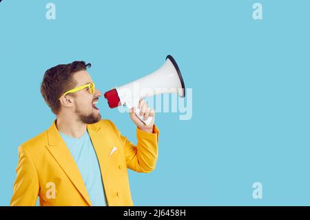 Un jeune homme expressif utilisant le mégaphone annonce des remises et des ventes sur fond bleu clair. Banque D'Images