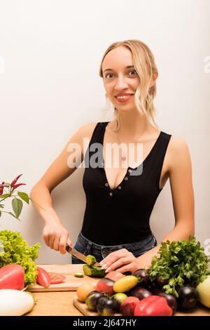 Jeune belle femme coupe des légumes avec un couteau dans la cuisine Banque D'Images