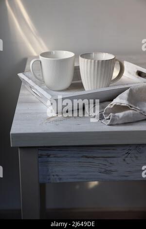 Deux mugs ondulés sur un plateau blanc et une serviette de cuisine sur une table beige contre un mur blanc. Style scandinave. Minimalisme. Placer pour le texte Banque D'Images