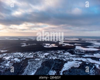 Vue épique aérienne d'hiver sur le village, la forêt et les champs couverts de neige. Région de Zmiyevsky en Ukraine de drone. Le soleil brille à travers de lourds nuages de coucher de soleil Banque D'Images