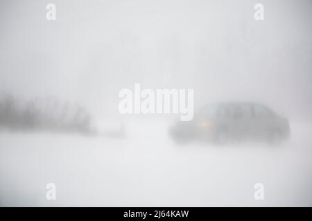 Voiture roulant sur une route enneigée pendant une tempête de neige aveuglante en hiver. Banque D'Images