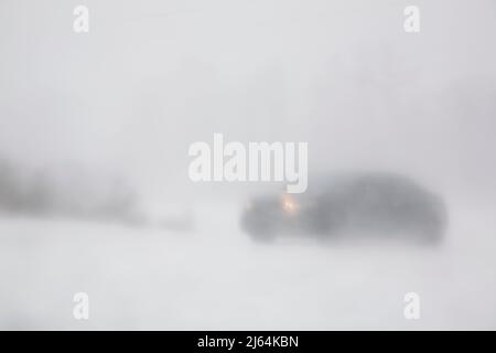 Voiture roulant sur une route enneigée pendant une tempête de neige aveuglante en hiver. Banque D'Images