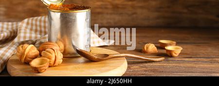 Boîte de conserve avec du lait concentré bouilli et de savoureux biscuits en forme de noix sur fond de bois Banque D'Images