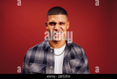 Un beau jeune homme qui se vante dans un studio. Jeune homme heureux regardant la caméra tout en se tenant debout sur un fond rouge. Jeune homme à la mode portant un e Banque D'Images
