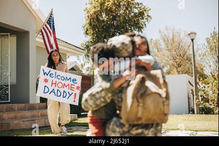 Soldat recevant un accueil chaleureux de sa famille. Un père militaire embrasse ses enfants après être revenu de l'armée. La réunitin d'un militaire américain Banque D'Images