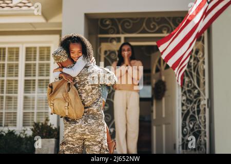 Soldat de l'armée embrassant sa fille après son retour à la maison. Un militaire américain surprend sa femme et sa fille à son retour. Militaire homme resuniti Banque D'Images