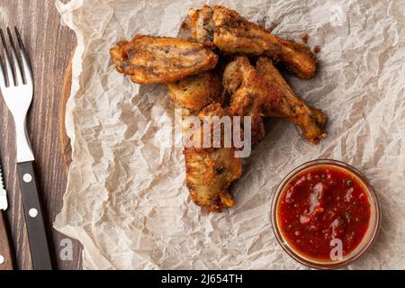 Ailes de poulet frites recouvertes d'une véritable sauce barbecue chaude, servies avec une sauce Chili chaude rouge sur un papier parchemin sur fond de bois Banque D'Images
