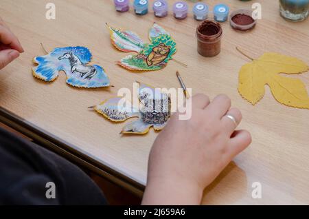 Les mains d'une femme adulte tiennent une brosse à peinture. Trois dessins d'animaux sont tirés sur les feuilles d'un arbre. Un hibou, un ours cub et un cheval. Banque D'Images