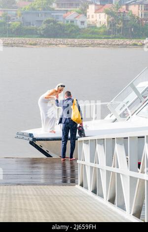 Juste marié Kieran aide sa nouvelle mariée Amy, pieds nus et sous la pluie, viennent à terre d'un bateau-taxi à Sydney sur leur chemin à leur réception Banque D'Images