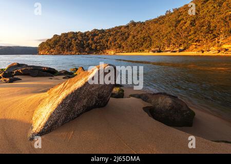 rochers sur une plage de sable près de l'eau avec lumière du soleil sur la tournière Banque D'Images