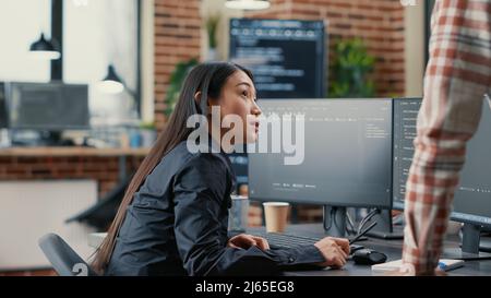 Développeur de base de données crayon de pointage à l'écran de l'ordinateur avec le logiciel de compilation de code expliquant l'algorithme source à un collègue debout à côté du bureau. Les ingénieurs système discutent du projet d'équipe ai. Banque D'Images