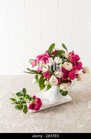 un beau bouquet de roses de jardin frais dans un vase décaratif sous forme d'arrosoir. table en béton contre un mur en brique blanche Banque D'Images