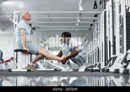 Portrait à vue latérale d'un jeune médic afro-américain examinant un homme senior à la salle de gym, espace de copie Banque D'Images