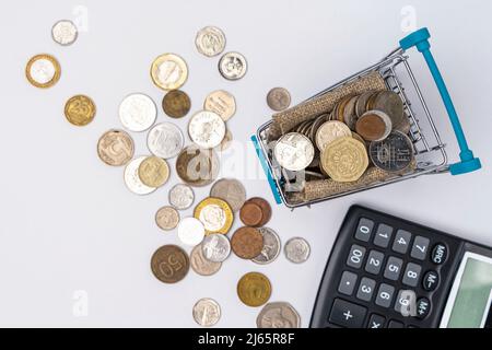 pièces dans un panier de supermarché et une calculatrice sur fond blanc Banque D'Images