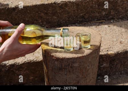 Un homme verse un brandy serbe traditionnel appelé rakija dans un petit verre spécial en plein air sur une bûche en bois Banque D'Images