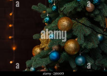 Gros plan d'un sapin de Noël à la décoration festive avec des boules bleues et dorées sur un fond de fée étincelant et flou. Guirlande lumineuse défocuée, Boke Banque D'Images