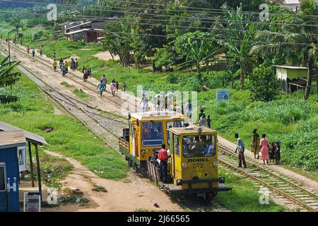 Ghana - chemin de fer entre Accra et la ville portuaire de Tacoradi. Les gens se promou par-dessus la voie pendant qu'une locomotive de maintenance vérifie les rails. Banque D'Images