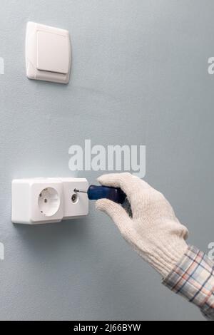 un homme dévisse avec un tournevis pour réparer une prise murale de télévision. Photo de haute qualité Banque D'Images