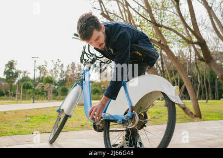 Jeune homme beau vérifie le pneu sur son vélo sur le parc de la ville. Banque D'Images