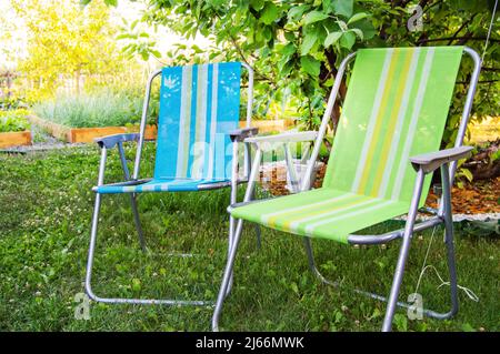 Deux chaises pliantes de jardin se tiennent à l'ombre sous un arbre lors d'une chaude journée d'été dans le jardin, en gros plan. Banque D'Images