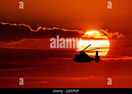 Un hélicoptère de la Garde côtière américaine vole en silhouette contre le soleil couchant dans une image composite. Banque D'Images