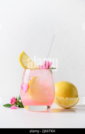 Boisson alcoolisée rose ou limonade, cocktail avec fleurs de rose et citron sur fond blanc ensoleillé. Gros plan. Format vertical. Banque D'Images