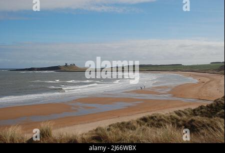 Image paysagée d'une large plage en courbe menant à un château de Dunstanburgh éloigné sur son affleurement de basalte sur la ligne d'horizon Banque D'Images