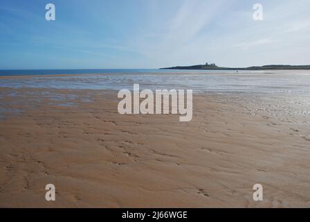 Image de style panoramique de la vaste plage ouverte d'Embleton Bay avec un château de Dunstanburgh éloigné sur sa crête de basalte et une figure isolée lointaine Banque D'Images