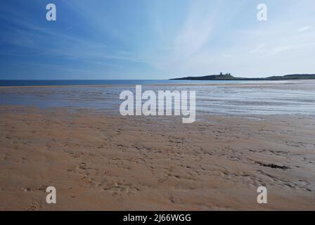 Image de style panoramique d'un château historique de Dunstanburgh à l'horizon, au premier plan de la large plage de sable et ouverte de la baie d'Embleton Banque D'Images