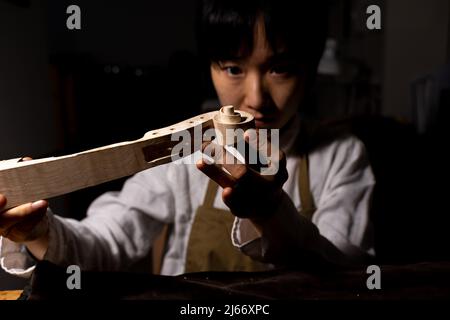 Jeune violoniste chinoise travaillant sur le cou du violon en construction dans son atelier Banque D'Images