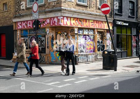 Les gens qui marchent le long de Brick Lane, à l'angle de Bacon Street, devant un magasin fermé couvert de graffiti dans l'est de Londres E1 Angleterre KATHY DEWITT Banque D'Images