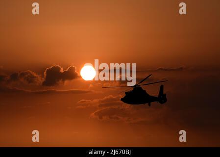 Un hélicoptère de la Garde côtière américaine vole en silhouette contre le soleil couchant dans une image composite. Banque D'Images