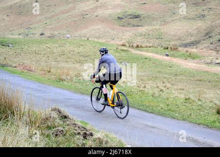 Un cycliste commence à monter sur le col HardKnott, l'un des cols abrupts de Lakeland que le défi Fred Whitton suivra. Il s'agit de l'une des nombreuses routes du Lake District, Cumbria, Angleterre, Royaume-Uni, sera fermée le 8th mai 2022, lorsque 2 500 cyclistes emprunteront la route Fred Whitton Challenge. Le défi Fred Whitton est un événement caritatif cyclosportif qui a lieu chaque année dans le district de English Lake. Il est tenu à la mémoire de Fred Whitton, secrétaire de course du Lakes Road Club, qui est décédé d'un cancer à l'âge de 50 ans en 1998. Banque D'Images