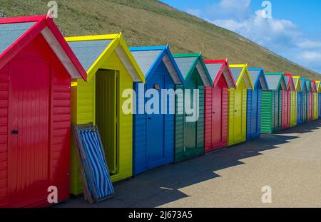 Rangée de cabanes de plage le long de la promenade de Whitby sur la côte du North Yorkshire, Royaume-Uni. Une chaise longue est penchée contre l'une des cabanes. Banque D'Images