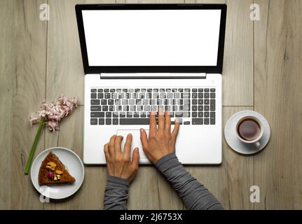 Vue de dessus des mains travaillant sur un ordinateur portable avec écran blanc et café sur le lieu de travail. Banque D'Images