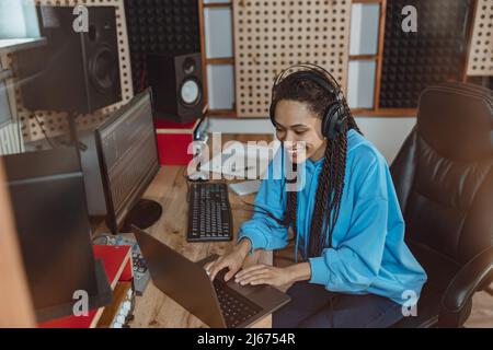 Ingénieure du son afro-américaine joyeuse travaillant sur un ordinateur portable dans le studio d'enregistrement du son Banque D'Images