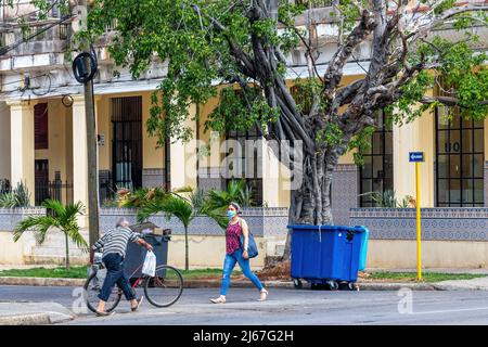 Un homme âgé pousse son vélo tandis qu'une jeune femme cubaine marche en portant un masque facial dans l'avenue Linea. Banque D'Images