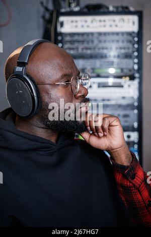 Portrait d'un homme noir sérieux et mûr avec barbe sur le visage travaillant en studio d'enregistrement à l'écoute de la piste Banque D'Images
