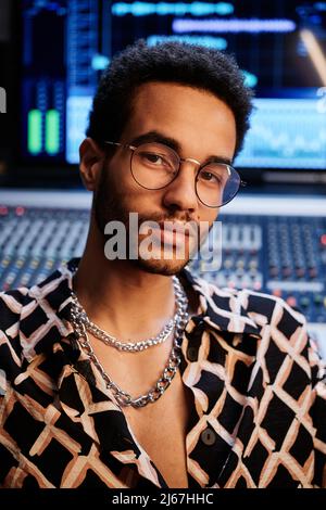 Gros plan d'un jeune garçon noir élégant portant une chemise tendance et des lunettes de vue travaillant en studio d'enregistrement Banque D'Images