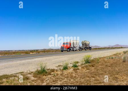 Semi-camion rouge tirant une double remorque sèche en vrac sur une route rurale dans le désert de Mojave Banque D'Images