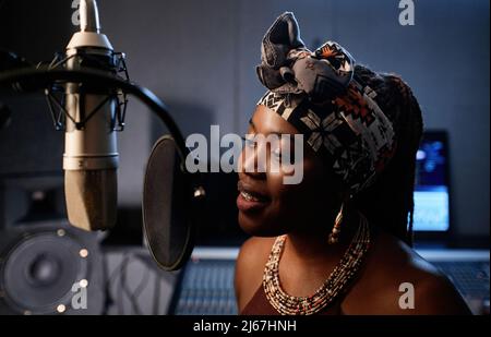 Portrait d'une jeune chanteuse afro-américaine élégante debout devant la chanson de chant du microphone dans un studio d'enregistrement Banque D'Images
