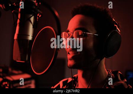 Gros plan du beau jeune chanteur noir debout devant la chanson de chant du microphone dans le studio d'enregistrement Banque D'Images