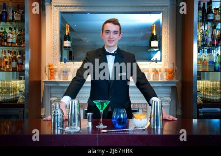 Barman debout derrière un verre au comptoir de bar d'un hôtel de luxe Banque D'Images