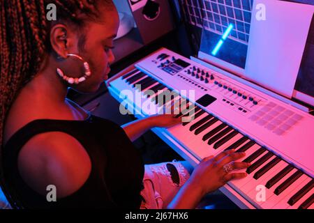 Prise de vue en grand angle de jeunes musiciens afro-américains jouant un clavier numérique dans un studio d'enregistrement, lumière néon Banque D'Images