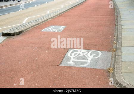 Piste cyclable marquée en rouge avec des symboles en forme de vélo peint sur asphalte le long d'une rue dans un centre-ville Banque D'Images