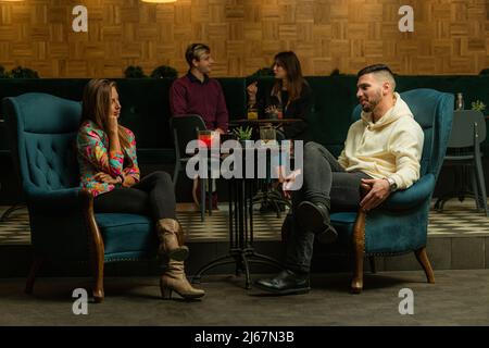 Deux merveilleux et beaux couples parlent les uns avec les autres tout en étant assis sur des tables différentes Banque D'Images