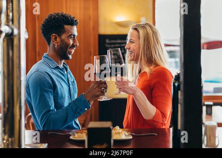 couple multiethnique célébrant avec un toast au vin rouge au bar d'une taverne Banque D'Images