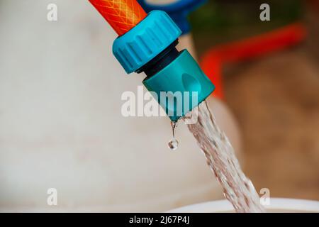 Un jet d'eau provenant d'un tuyau remplit un fût en plastique. Image d'arrière-plan. Le concept de la crise de l'eau potable dans le monde. Banque D'Images